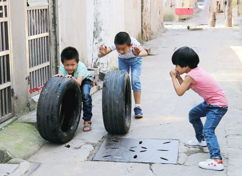 《童趣》十邓志安十18306128951十在横山桥老巷，三个小孩在玩着滚轮胎的游戏。.jpg